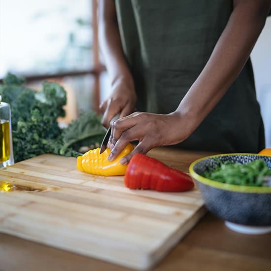A person slices a yellow pepper beside fresh vegetables