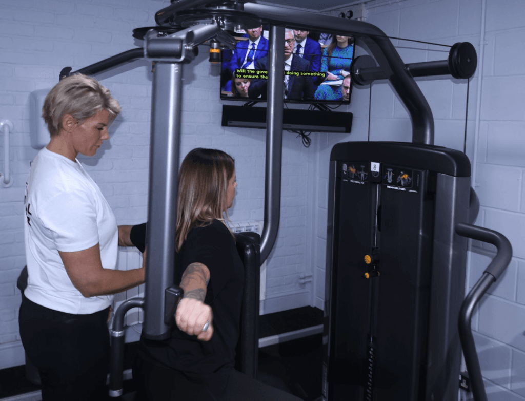Two people use a resistance-training machine in a gym